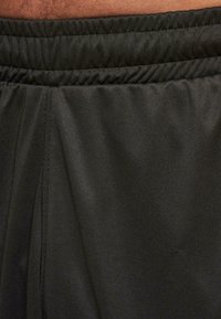 Black athletic shorts with a gathered waistband, smooth texture, and subtle sheen, featuring stitching details along the sides.