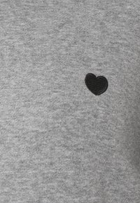 Felpa grigia realizzata in tessuto morbido con un piccolo cuore ricamato nero sul davanti.