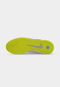 Φωτεινή κίτρινη υφή πέλματος παπουτσιού Nike με γκρι λογότυπο swoosh και ένα μικρό μπλε εξαγωνικό στοιχείο κοντά στη φτέρνα.