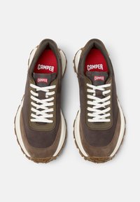 Braune und beige Sneaker mit weißen Schnürsenkeln und einem roten "CAMper"-Logo, die von oben auf einem hellen Hintergrund mit einer strukturierten Sohle dargestellt werden.