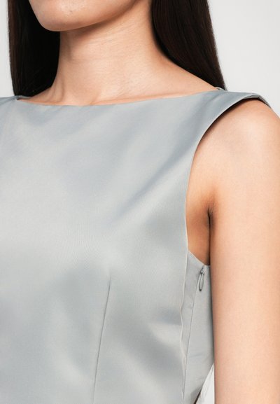 Világosszürke selyemruha ujjatlan kialakítással, kerek nyakkivágással és oldalsó zipzárral. Az sima textúra és az alakra szabott fazon kiemeli a letisztult vonalait.