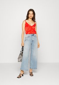Top de alças vermelho em V com um padrão de riscas de tigre, emparelhado com jeans de perna larga de cintura alta em azul claro. Acessorizado com uma mala de padrão de zebras e sapatos de salto pretos.