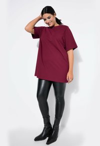Camiseta oversized burdeos de manga corta combinada con leggings de piel sintética negra y botines de punta con tachuelas metálicas.