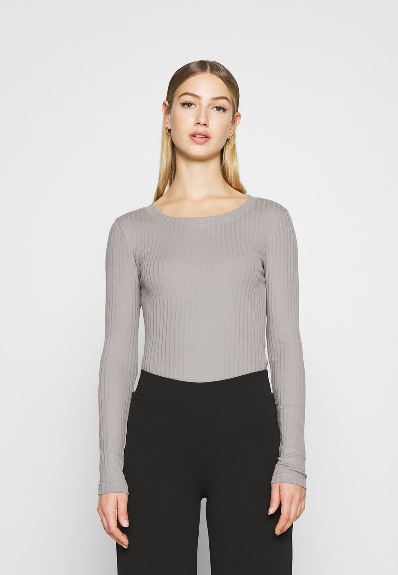 Long-sleeve, lightweight top in light gray with a ribbed texture, featuring a scoop neckline and fitted silhouette. Paired with black pants.