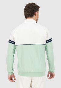 Mintgrønn genser med hvit øverste del og marineblå stripe detaljer. Har raglanermer og ribbestrikket kant. Glatt tekstur.