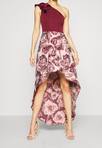 Asymetryczna sukienka z bordowym gorsetem i kremową spódnicą ozdobioną kwiatowym wzorem w odcieniach różu i bordo; nierówny, wysoki przód i długi tył.