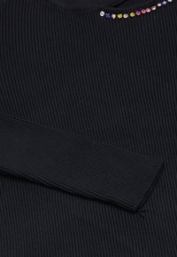 Top negru cu maneci lungi și dungi, având un decolteu rotund și pietre decorative colorate de-a lungul decolteului. Materialul texturat amplifică adâncimea.