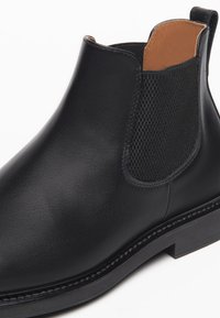 Stivale alla caviglia in pelle nera con pannelli elasticizzati testurizzati, finitura liscia, tacco basso impilato e rivestimento in pelle marrone a contrasto.