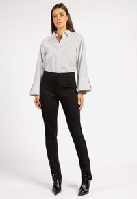 Gestreept button-up shirt met uitlopende mouwen, gecombineerd met zwarte aansluitende broeken met zijknopen en een gladde textuur.