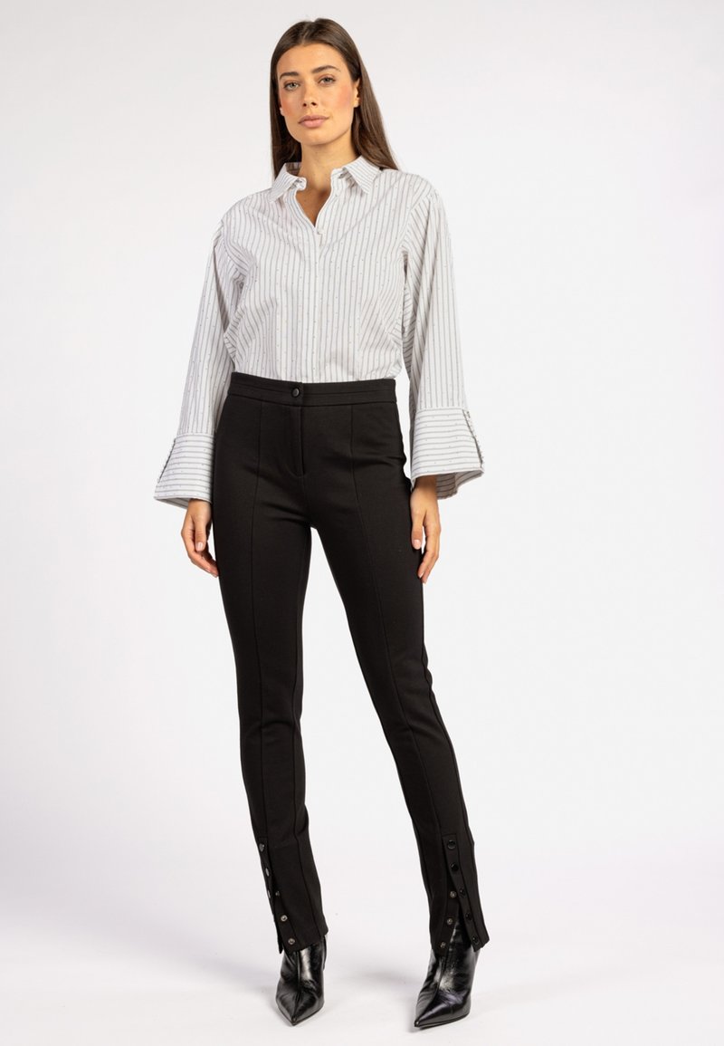 Gestreept button-up shirt met uitlopende mouwen, gecombineerd met zwarte aansluitende broeken met zijknopen en een gladde textuur.
