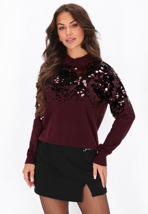 Pulover str burgund cu embellishments din paiete pe umeri, asortat cu o fustă neagră cu o fanta pe lateral și detalii cu fermoar.