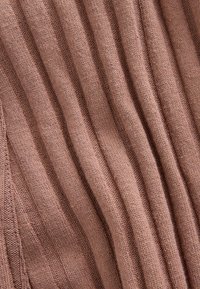 Ribbad stickad tyg i mjuk mauve med texturerade vertikala linjer, som visar en jämn yta och subtila variationer i tjocklek.