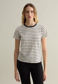 T-shirt a righe con strisce nere su uno sfondo crema, scollo tondo con bordino nero, maniche corte e forma aderente.