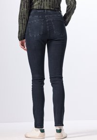 Jeans ajustados de color azul oscuro con una altura media, dos bolsillos traseros y una textura clásica de denim. Combinados con zapatos blancos que presentan un acento verde.