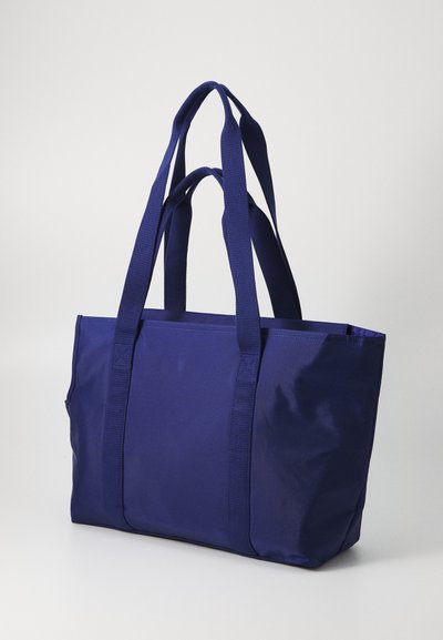 Navy blue tote bag made of durable fabric, featuring two thick handles and a spacious, open-top design. Smooth texture, no visible embellishments.
