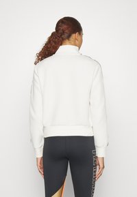 Hvit hettegenser med høy krage, ribbet nederkant og mansjetter. Har svarte side-striper langs ermene. Kombinert med svarte leggings.
