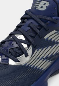Chaussure de sport marine avec une tige en mesh texturé, des accents argentés et des détails rayés dimensionnels. Les lacets passent à travers des oeillets renforcés.