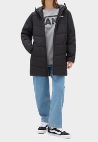 Czarna, puchowa kurtka z kapturem, zamkiem błyskawicznym i widocznymi szwami. Nosi się ją na szarą bluzę i zestawia z jasnoniebieskimi dżinsami oraz czarnymi trampkami.