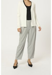 Cardigan beige chiaro realizzato in materiale morbido, abbinato a una canotta nera e pantaloni larghi grigio chiaro. Tacchi neri a punta completano il look.