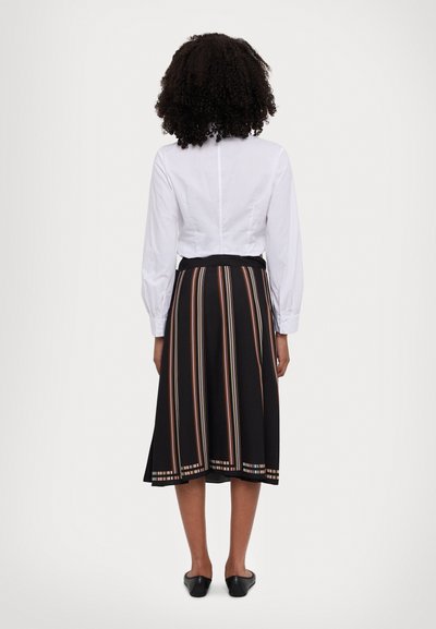 Falda negra con rayas verticales multicolores, textura suave y un dobladillo con patrón. Camisa blanca de manga larga con un diseño ajustado.