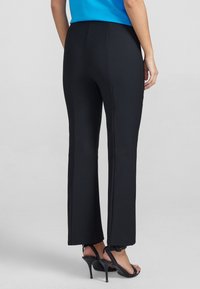 Czarne, rozszerzane spodnie wykonane z elastycznego materiału, z wysokim stanem i gładką fakturą, zestawione z czarnymi sandałami na wysokim obcasie.