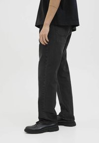 Vaqueros de denim negros con corte recto, detalles de costura sutiles y un acabado texturizado, combinados con zapatos negros de cordones.
