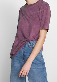 Kortärmad t-shirt med rund hals i urtvättad lila bomull. Avslappnad passform, något sliten textur. Kombinerad med högmidjade blåjeans.