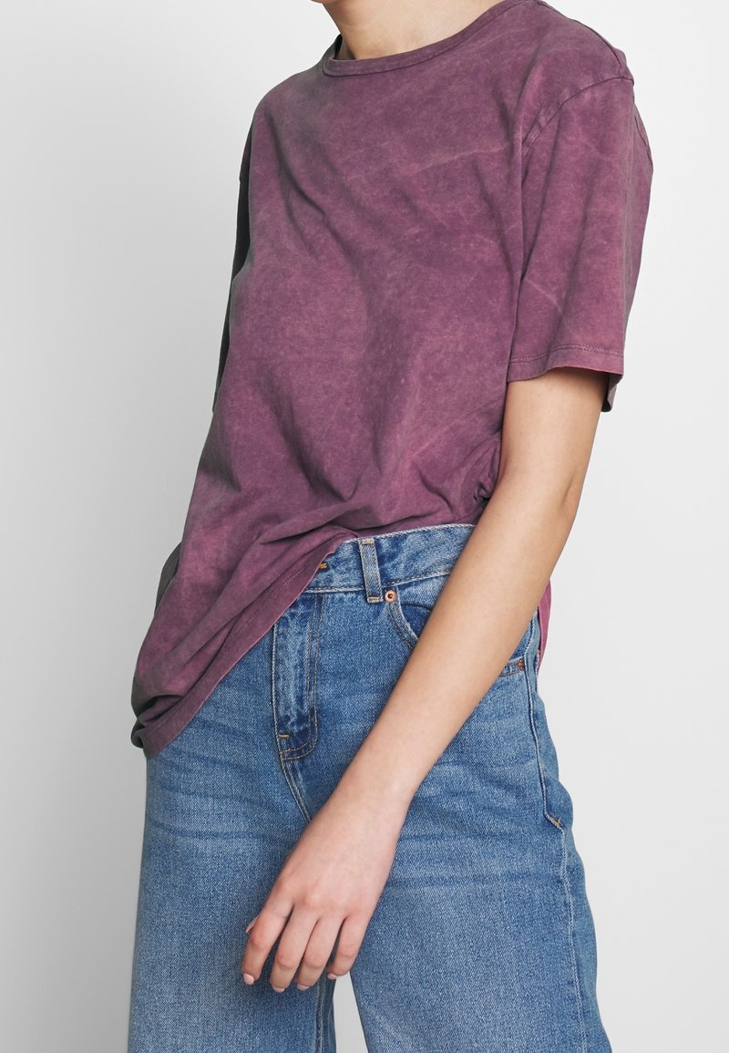 Kortärmad t-shirt med rund hals i urtvättad lila bomull. Avslappnad passform, något sliten textur. Kombinerad med högmidjade blåjeans.