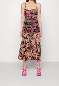 Woman wearing a sleeveless floral dress with pink, green, and beige patterns, paired with bright pink strappy high-heeled sandals.