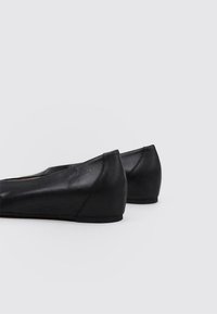 Bailarinas de cuero negro con un diseño elegante, punta redondeada, tacón bajo y una sutil marca en el tacón. Textura suave, estilo minimalista.