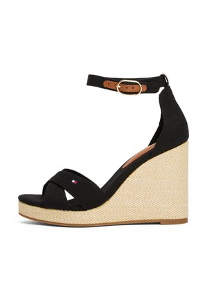 Sandalias de cuña negras con tiras cruzadas de lona, correa ajustable en el tobillo con acento de cuero marrón y tacón de cuña de fibra natural texturizada.