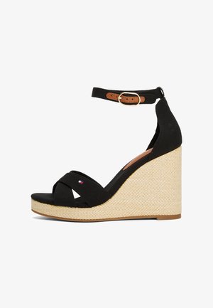 Sandales compensées noires avec des brides croisées en toile, bride de cheville ajustable avec un accent en cuir marron, et un talon compensé en fibres naturelles texturées.