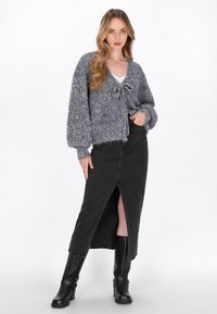 Cardigan in maglia spessa blu e grigio con legatura frontale, abbinato a una gonna di jeans nera con uno spacco frontale e stivali neri al ginocchio.