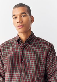 Camicia a quadri rossi e verdi con bottoni e colletto, dotata di taschino sul petto e etichetta del marchio sul lato. Realizzata in tessuto intrecciato.