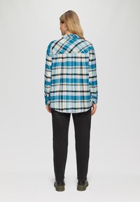 Camicia a quadri con colletto in blu, bianco e nero, caratterizzata da una vestibilità comoda e maniche lunghe. Abbinate a pantaloni neri e robusti stivali verdi.