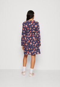 Blommig klänning med långa ärmar, marinblå bakgrund, röda och vita blommor, rynkad midja, flervåningskjol, kombinerad med sneakers och vita strumpor.