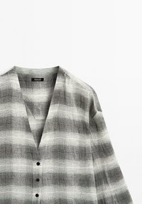 Knoopshirt van een lichtgewicht stof, met een grijs-witte geruite patroon, een diepe V-hals en korte mouwen.