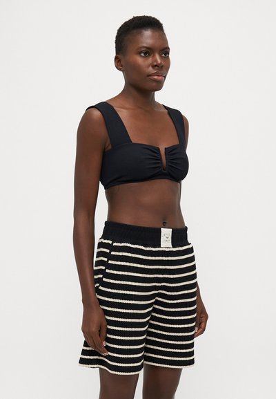 Crni rebrasti crop top s širokim naramenicama, središnjim prorezom. Uparen s crno-bijelim prugastim pletenim šortsem s elastičnom gumom.