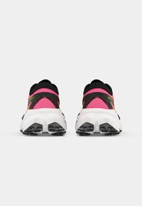Une paire de chaussures de course rose et noire avec de grosses semelles blanches, vues de l'arrière sur un fond blanc uni.