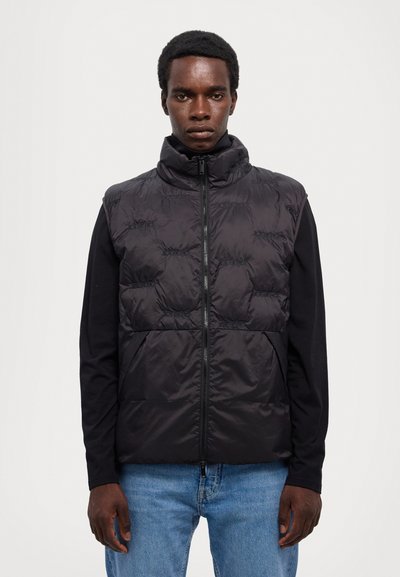 Μαύρο γιλέκο με φουσκωτό σχέδιο, υψηλό γιακά, φερμουάρ μπροστά και ραφές. Συνδυασμένο με μαύρη μπλούζα μακρυμάνικη και μπλε τζιν.