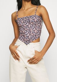 Blommig kort topp med tunna band, med en mörkblå bakgrund och rosa, vita och gröna blommönster. Strukturerad tyg, åtsittande design.