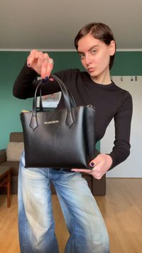 Svart skinnhåndveske med en strukturert silhuett, korte håndtak og gullfarget logodetalj, vist mot en nøytral bakgrunn.