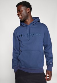 Felpa blu navy realizzata in tessuto morbido, con tasca a marsupio e logo "Champion" ricamato in tonalità a contrasto.