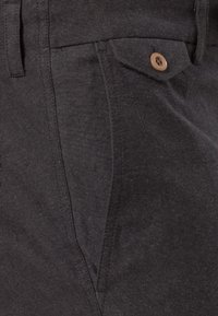 Svarta byxor av texturerat tyg med framfickor, bruna knappstängningar och rak design på benen.