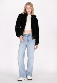 Jachetă neagră pufoasă cu fermoar, cu guler înalt, asortată cu blugi evazați de culoare albastru deschis și adidași albi. Design simplu și textură moale.