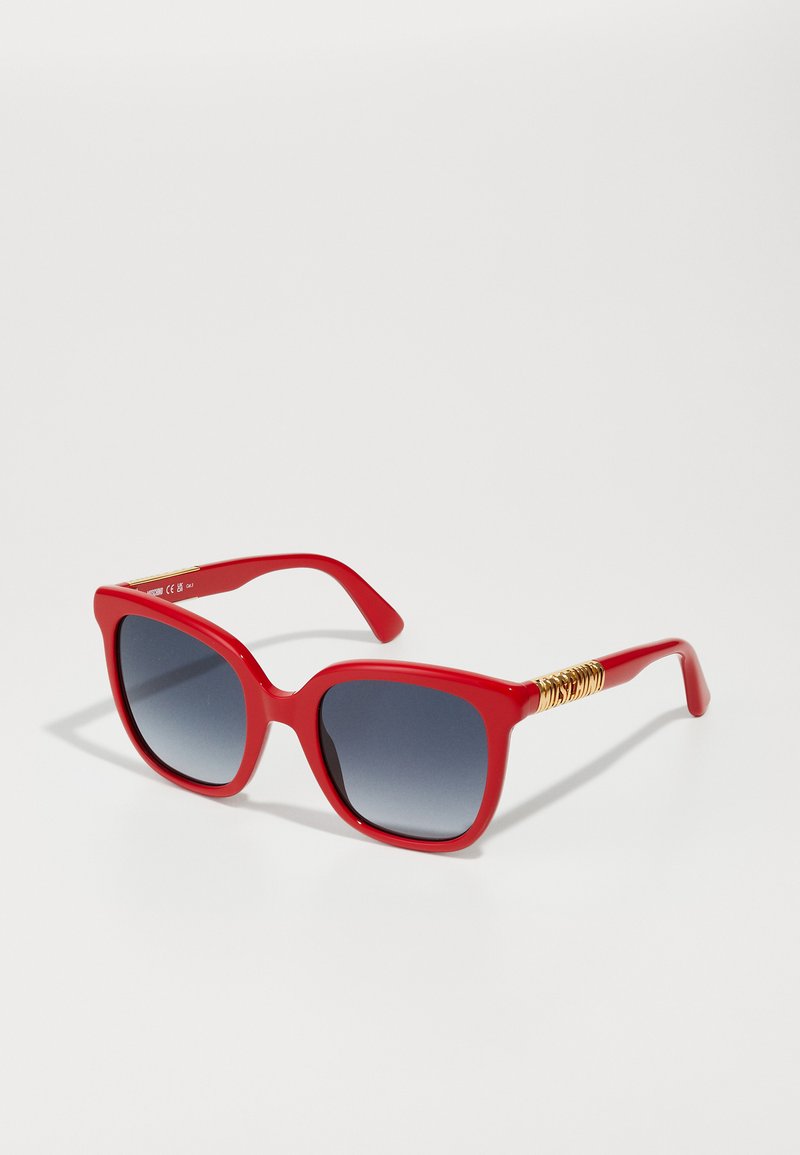 Ochelari de soare din plastic roșu cu rame pătrate, lentile gri cu gradient și accent de aur pe brățară, având o textură netedă și lucioasă.