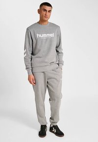 Grå sweatshirt och mjukisbyxor i bomullsblandat material, med en logotyp, ribbade muddar och design med tre ränder på ärmarna.