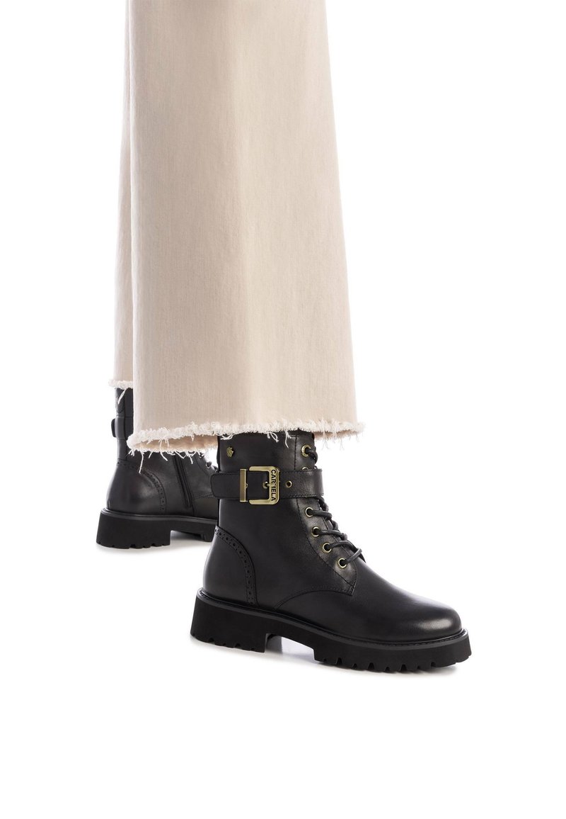 Botas de tobillo de cuero negro con detalle de hebilla, diseño de cordones, suela texturizada y acabado mate con punta redonda.