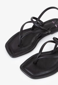 Zwarte platte sandalen met een vierkante teenontwerp en dunne kruissandalenbandjes. Gemaakt van soepel materiaal met een strakke, minimalistische esthetiek.
