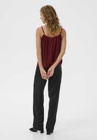 Bordo bezrukavni top s nabranim izrezom u kombinaciji s crnim širokim hlačama, koje imaju glatku površinu i opušteni kroj.
